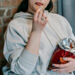 Crop plump female in casual hoodie enjoying crispy baked breads and licking lips against brick wall